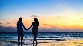 man and woman holding hands walking on seashore during sunrise